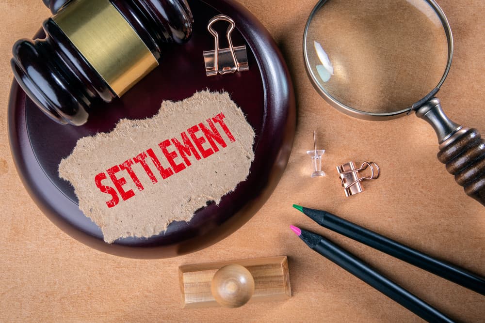 Word settlement on piece of paper with wooden court hammer and magnifying glass on the table