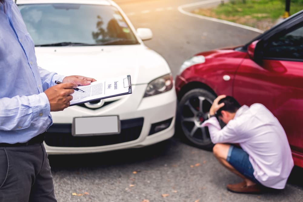Insurance agent writing on clipboard while examining car after accident claim being assessed and processed.